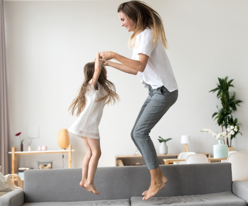 Woman and girl holding hands and jumping on sofa