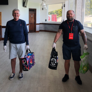 Two men inside a hall wearing disposable gloves and carrying food bags