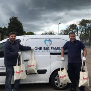 Two man standing by a van wearing disposable gloves and holding bags of food.