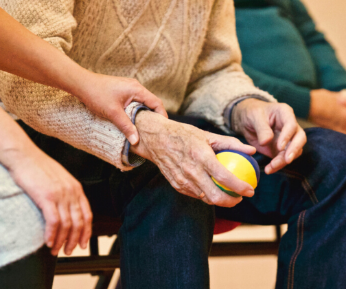older person sitting in chair, holding ball in his hand
