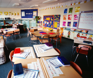 Empty primary school classroom with tables laid out and colourful displays on the walls.