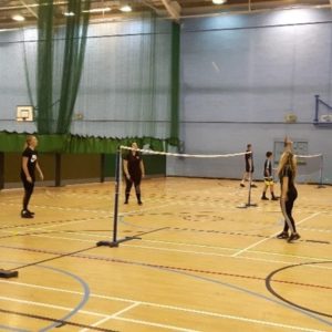 Teenage children playing badminton in a school sports hall.